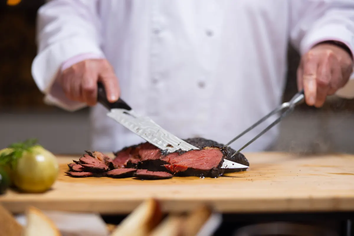 Chef David Teyf carving smoked pastrami on a wooden board